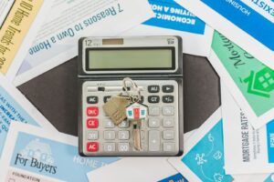 Calculator and a set of house keys resting on property purchase documents on a desk