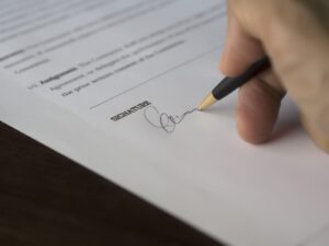 Close-up of a hand signing a printed document with a pen on a wooden desk
