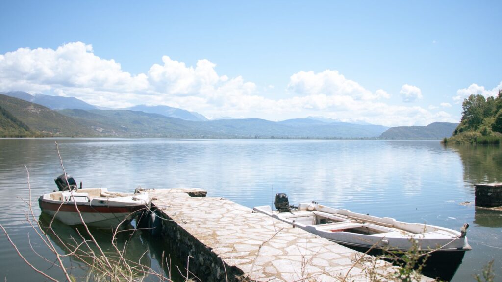 Boats moored at a stone pier on the lake in Ioannina, with mountains behind