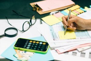 Office desk with paperwork, a calculator and glasses as a person writes notes