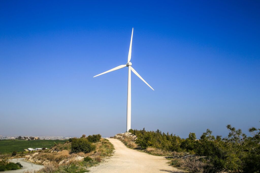 White wind turbine under a clear blue sky beside a country path
